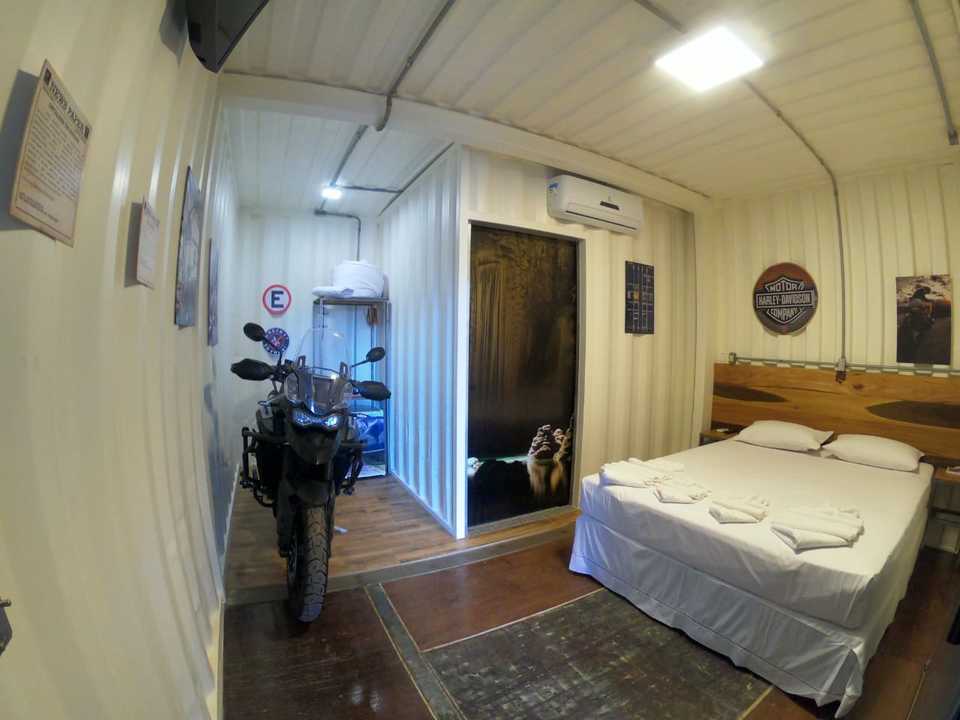 Apartamento MotoBox térreo com moto ao lado da cama de casal